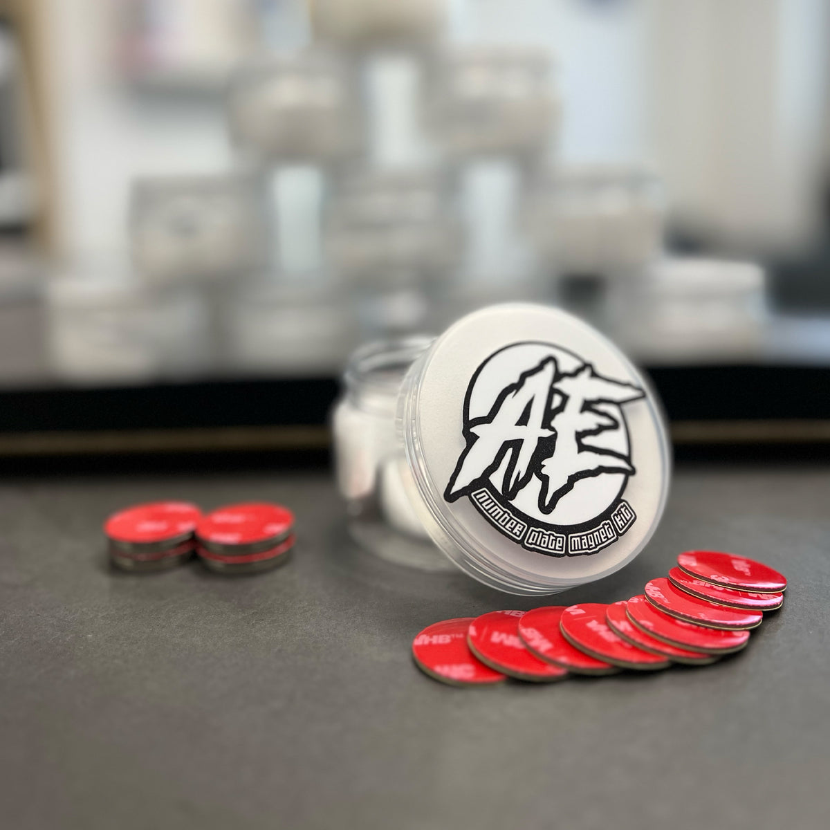 A number plate magnet kit displayed with red circular magnets in front of a clear container with a silver lid featuring a white logo.