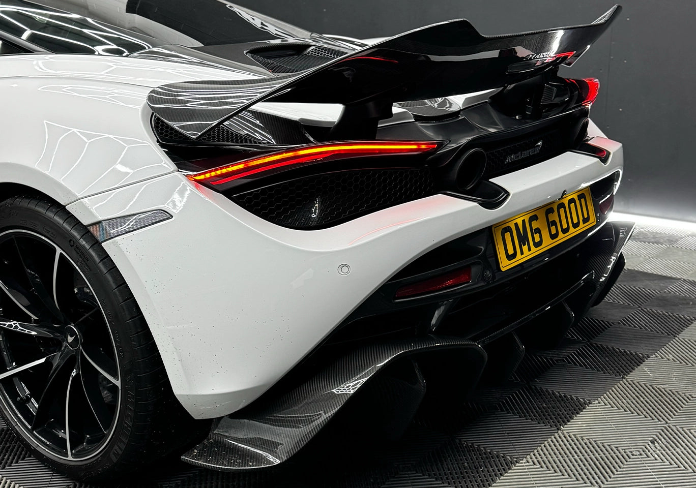 White McLaren 720S with a carbon fibre rear wing and diffuser on a checkered floor.